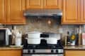Kitchen with wooden cabinets, stainless steel stove, white pots, cutting boards, and a small plant on the counter.