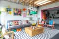 Colorful living room with gray sofa, vibrant cushions, striped rug, wooden coffee table, and eclectic wall art.