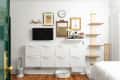 Living room with wall-mounted TV, white cabinets, framed art, and a wooden shelf.
