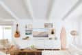Living room with white walls, a guitar, surfboard, framed art, and a wicker floor lamp.