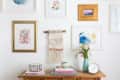Gallery wall with framed art, macramé hanging, wooden console, books, vase with flowers, and a small clock.