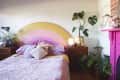 Bedroom with rainbow headboard, pink quilt, colorful pillows, plants, and a pink fireplace with unicorn decor.