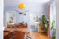 Dining room with wooden table, chairs, yellow pendant light, large plant, and colorful oars on the wall.