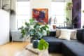 Living room with dark gray sectional sofa, abstract art, and lush green plants near windows.