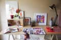 Creative workspace with colorful art supplies, framed artwork, desk lamp, and a plant on a wooden desk.
