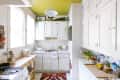 Bright kitchen with white cabinets, yellow ceiling, colorful rug, and plants on countertops and shelves.