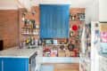 Kitchen with exposed brick, blue cabinets, marble countertop, hanging pots, and a fridge covered in magnets and notes.