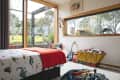 Child's bedroom with dinosaur-themed bedding, a red blanket, toy guitar, and a yellow toy cart filled with toys.