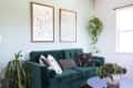 Green velvet sofa with patterned cushions, abstract line art, and hanging plants in a bright living room.
