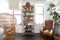 Rattan chair, cowhide armchair, and bookshelf with decor items in a bright room with potted plants.