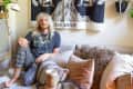 Person with long hair sitting on a sofa with plaid pants, surrounded by pillows and a tapestry labeled "The Moon."