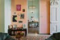 Eclectic living room with art-covered peach wall, record player, and view into a mint green office with a desk and stool.