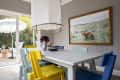 Dining room with colorful chairs, white table, large pendant light, and framed fox artwork on gray paneled wall.