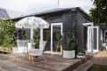 Patio with wicker chairs, floral umbrella, potted cacti, and ivy-covered black brick house.