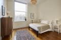 Minimalist bedroom with a wooden dresser, large window, woven pendant light, and a bed with beige bedding.
