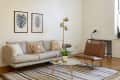 Living room with a gray sofa, brown chair, glass coffee table, striped rug, and plant decor. Two leaf prints on the wall.