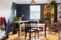 Dining room with black and white table, black chairs, yellow bookshelf, and potted plants near a window.