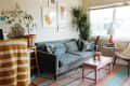 Cozy living room with a gray sofa, colorful rug, plants, and a pink coffee table with decor items.