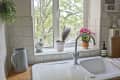 Kitchen sink with silver faucet, potted plants on windowsill, and soap dispenser on tiled counter.