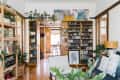 Living room with wooden shelves filled with plants, books, and decor, leading to a dining area with a table and chairs.