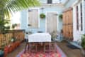 Outdoor patio with a floral tablecloth, wooden chairs, potted plants, and string lights against a light blue house.