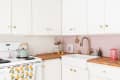 White kitchen with pink subway tile backsplash, brass faucet, mint kettle, and citrus-patterned towel on stove.
