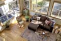 Cozy living room with brown sectional sofa, patterned pillows, wooden chair, plants, and a rustic coffee table on a patterned rug.