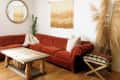 Rust-colored sectional sofa in living room with wooden coffee table, round mirror, wall hanging, and pampas grass decor.