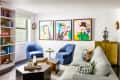 Modern living room with blue chairs, abstract art, gray sofa, and bookshelves.
