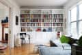 Living room with a large bookshelf filled with colorful books, gray sectional sofa, glass coffee table, and a potted plant.