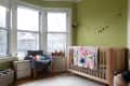 Nursery with green walls, wooden crib, colorful quilt, gray chair, and moon phase wall decor.