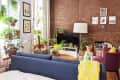 Cozy living room with brick wall, blue sofa, yellow throw, TV, and numerous potted plants on shelves and tables.