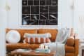 Tan leather sofa with textured pillows and a gray throw, under a space-themed wall art. Coffee table with books and candles.