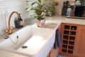 Farmhouse kitchen sink with brass faucet, floral plant, wooden cabinets, and patterned tile floor.