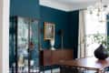 Dining room with teal walls, glass cabinet, wooden sideboard, framed art, and a modern chandelier.