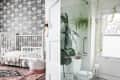Nursery with floral wallpaper, white crib, and patterned rug; bathroom with glass shower, plants, and window.