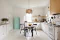 Bright kitchen with white cabinets, wooden table, black chairs, mint green cabinet, and a pendant light fixture.