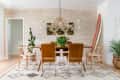Dining room with a wooden table, brown chairs, wicker pendant light, plants, and a surfboard against a textured wall.
