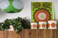 Retro kitchen decor with green and orange floral canisters, leafy plant, and a vibrant wall art piece above wooden cabinets.