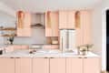 Modern kitchen with pink cabinets, white countertops, copper pendant lights, and plants on the island.