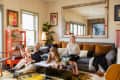 Family in a cozy living room with a gray sofa, orange shelf, large mirror, and colorful decor.