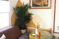 Cozy corner with a purple sofa, glass table, potted plant, and framed landscape painting.
