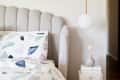 Gray upholstered headboard, geometric patterned bedding, white pendant light, and small vase on stacked books.