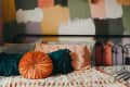 Bed with colorful abstract wall, orange round pillow, green and pink cushions, and a crocheted blanket.
