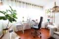 Home office with a desk, black chair, large plant, and bookshelf, featuring a computer and decorative items.