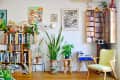 Living room with bookshelves, potted plants, colorful artwork, a stereo system, and a yellow armchair.