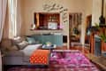 Cozy living room with gray sofa, orange polka dot blanket, pink rug, and bat wall decals near a kitchen entrance.