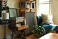 Cozy living room with a blue chair, leafy pillow, record player, and potted plant near a window.