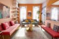 Colorful living room with orange walls, pink sofas, abstract art, and a round gold coffee table.