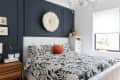 Bedroom with black and white floral bedding, orange pillow, dark accent wall, and white feather wall decor.